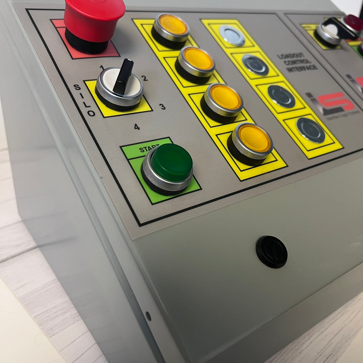 Close-up of an industrial control panel with multiple push buttons, including red, yellow, green, and silver buttons, on a gray metal housing.