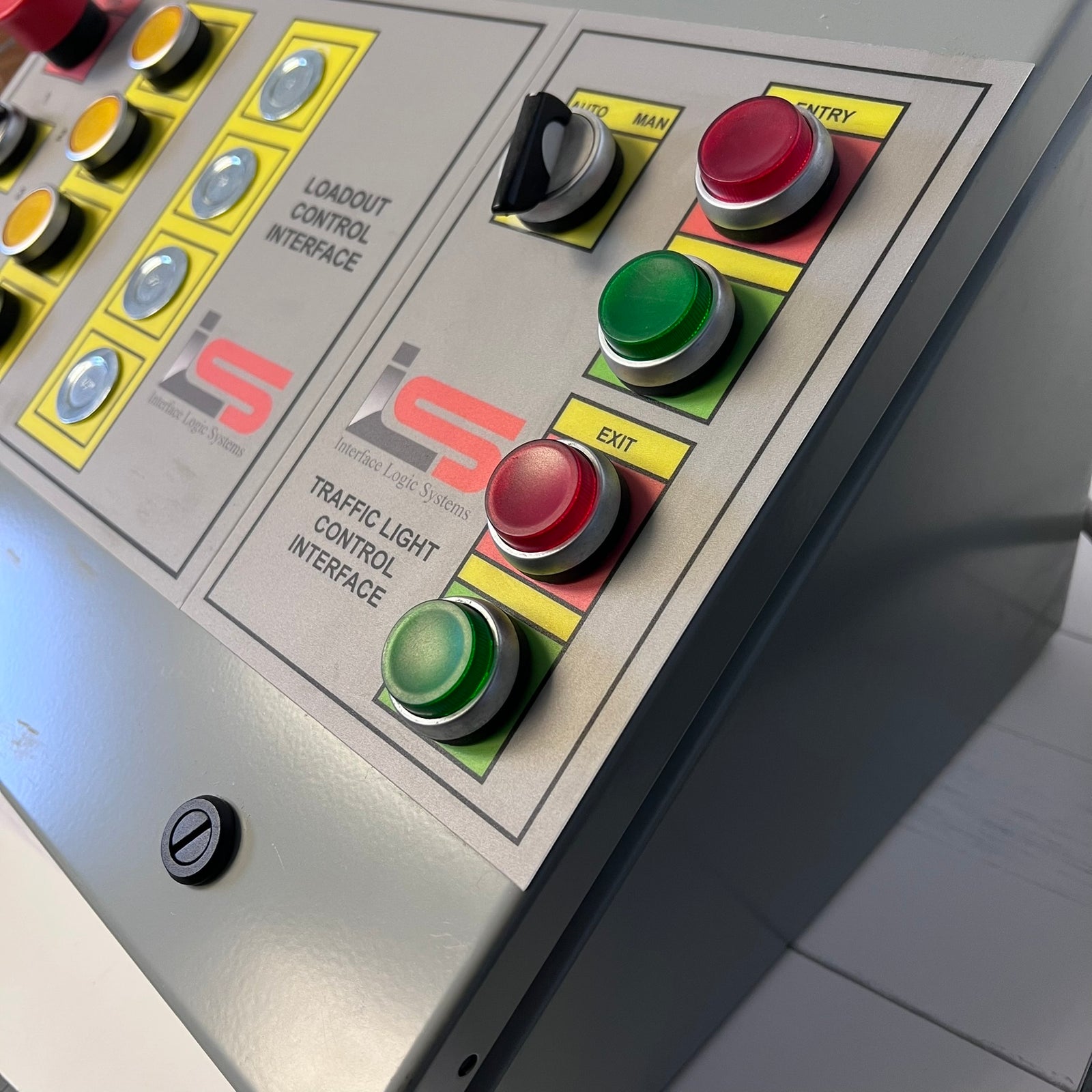 Close-up of a gray industrial control panel with red, green, and black buttons, yellow label areas, and printed interface text including 'LOADOUT CONTROL INTERFACE' and 'TRAFFIC LIGHT CONTROL INTERFACE'.